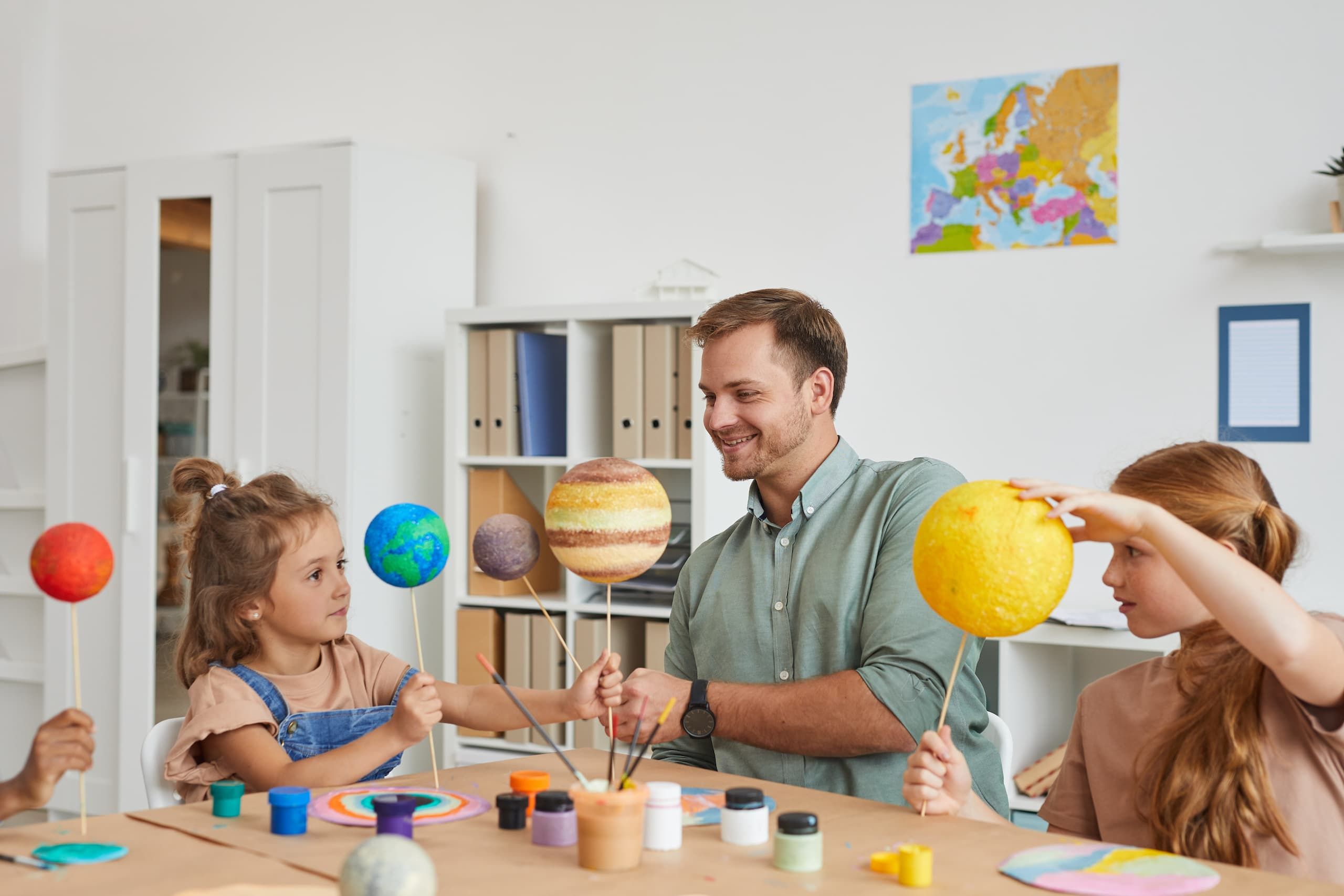 Father and two young daughters building solar system replica with foam balls